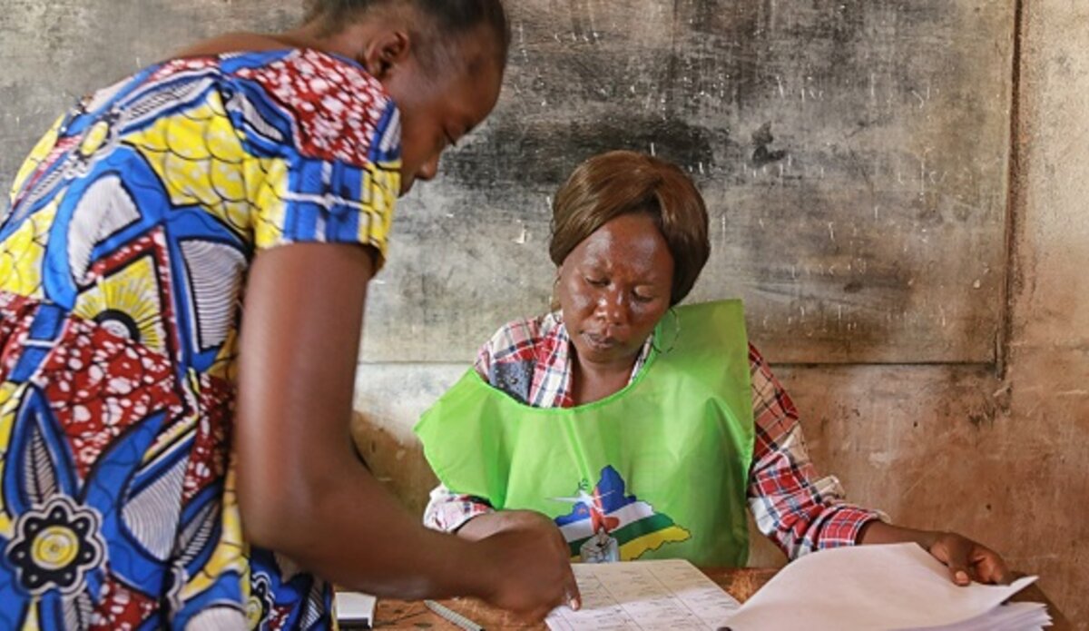 Un agent électoral (à droite) aide une électrice dans un bureau de vote lors de l'élection présidentielle en République centrafricaine.